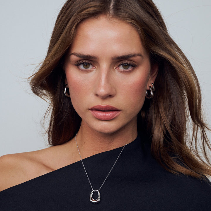Woman wearing a black one-shoulder top and silver necklace with a plain background
