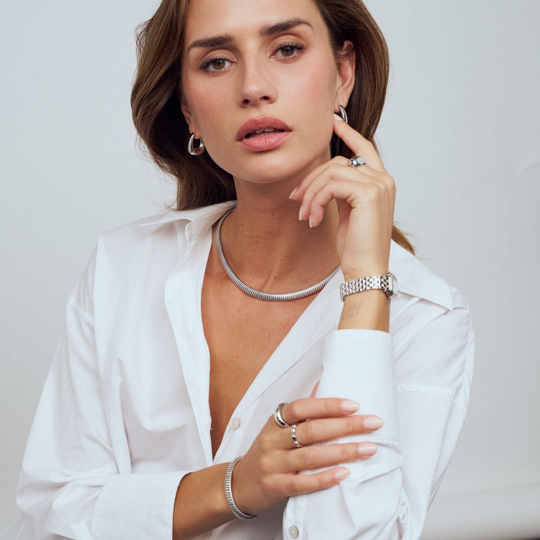 Woman wearing silver jewelry including a necklace, bracelet, and rings on a plain background