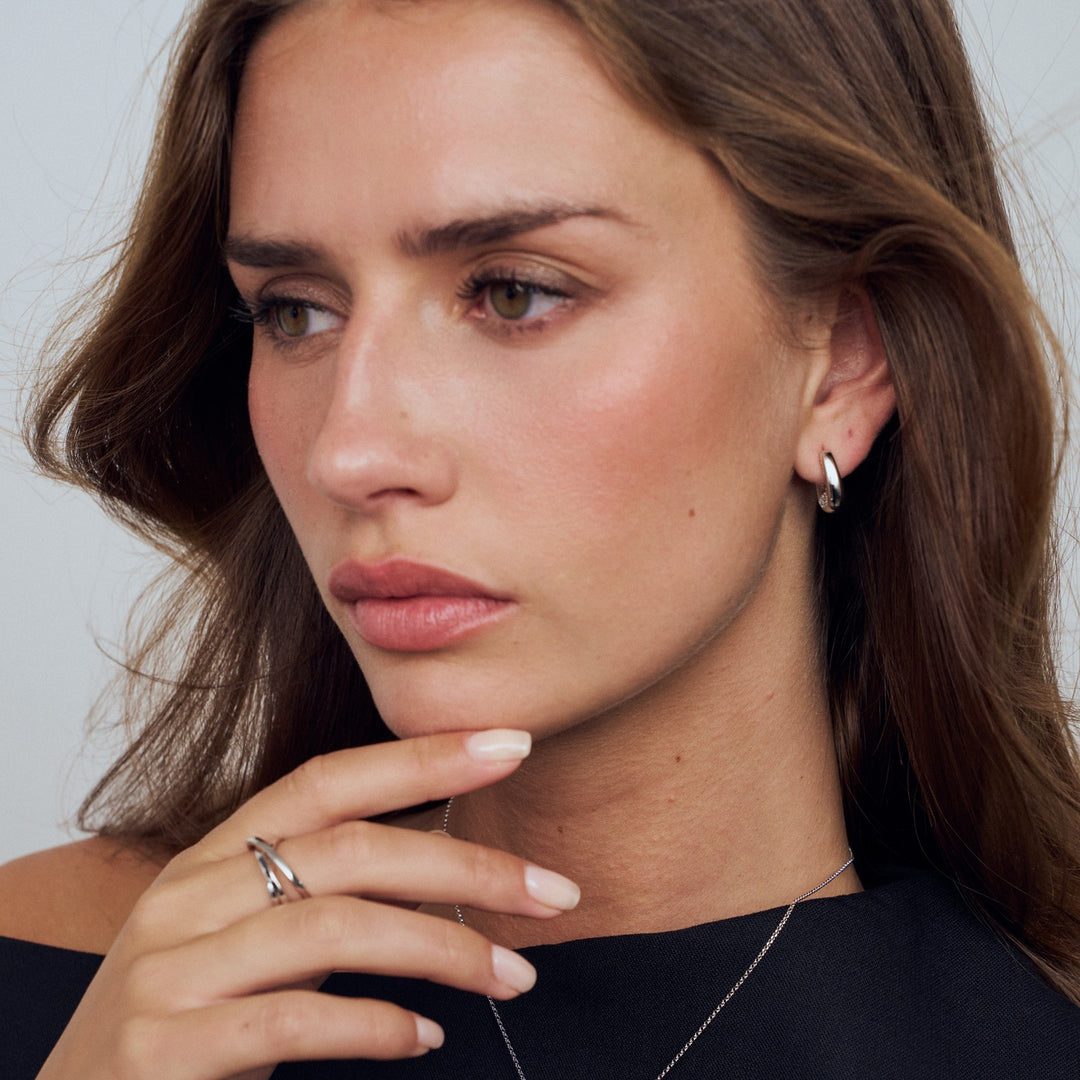 Close-up of a woman wearing earrings and a ring, with a neutral background