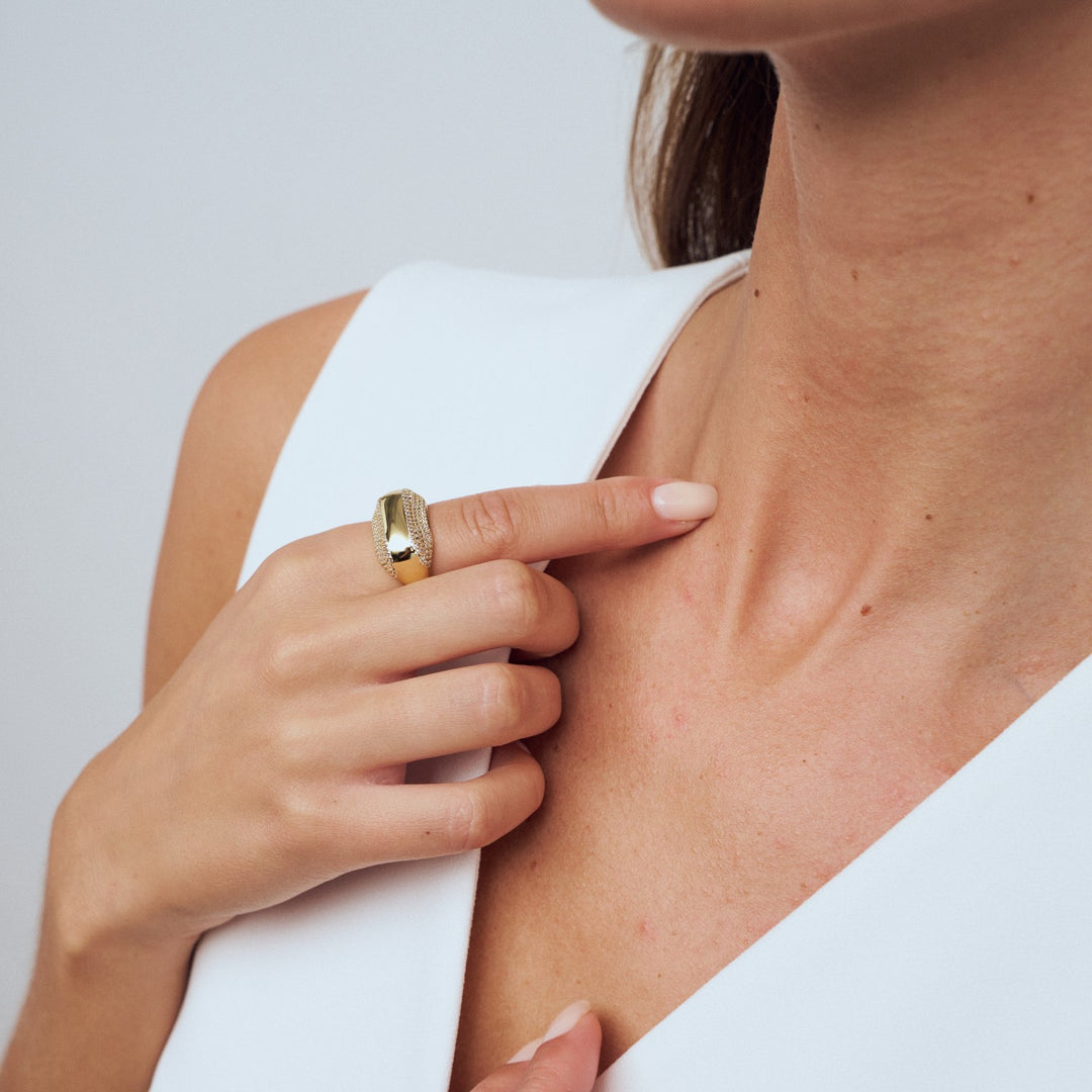 Close-up of a person wearing a gold ring on a plain background