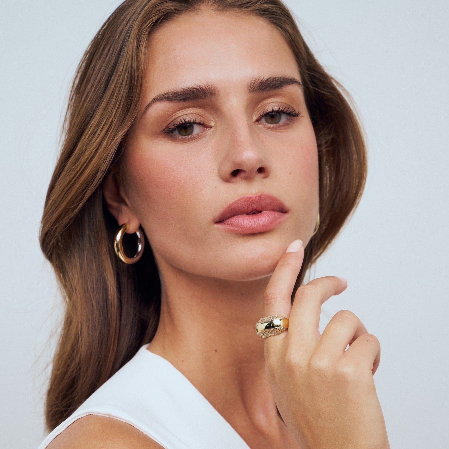 Woman wearing gold hoop earrings and a ring on a light background