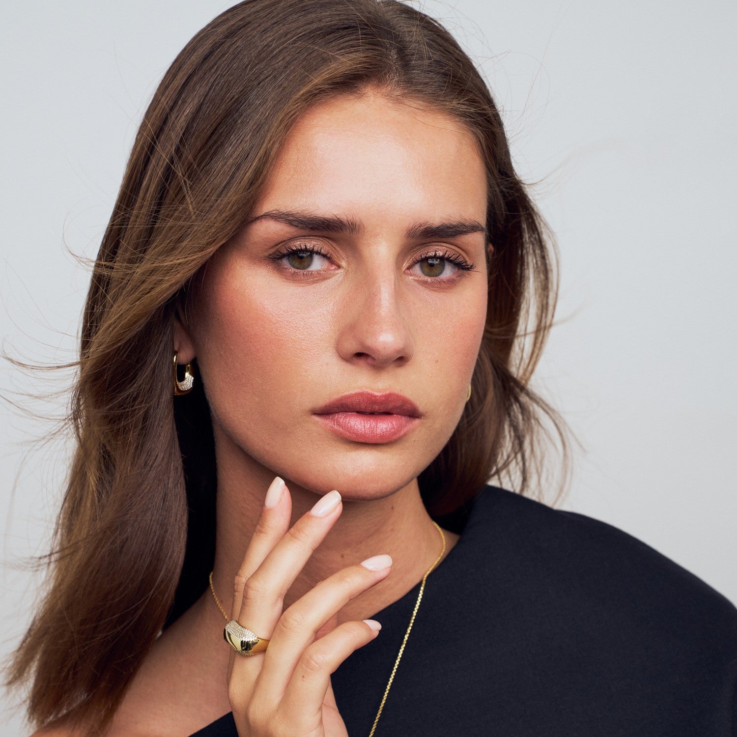 Woman with long brown hair wearing a black top against a plain background