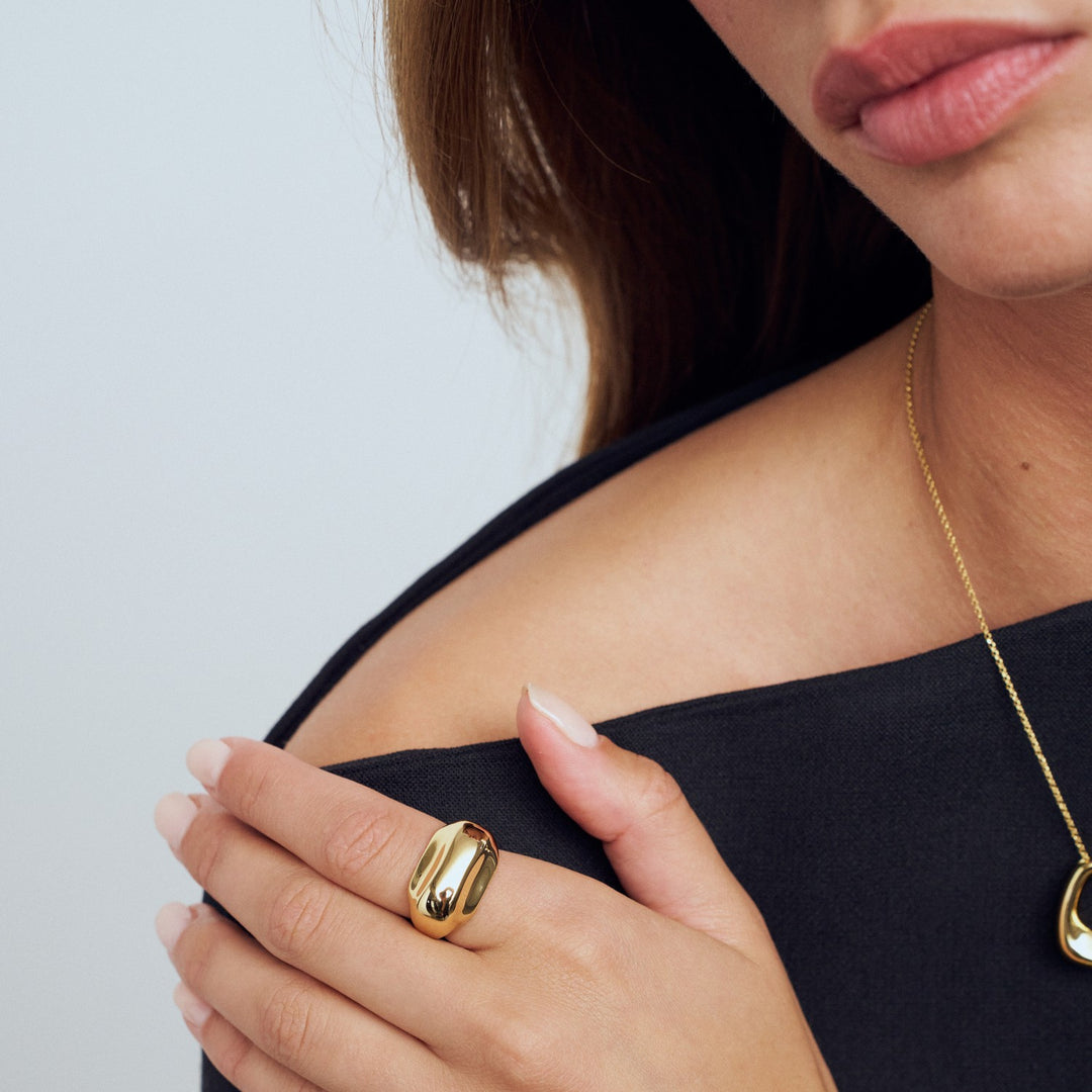 Woman wearing a gold ring and necklace on a plain background