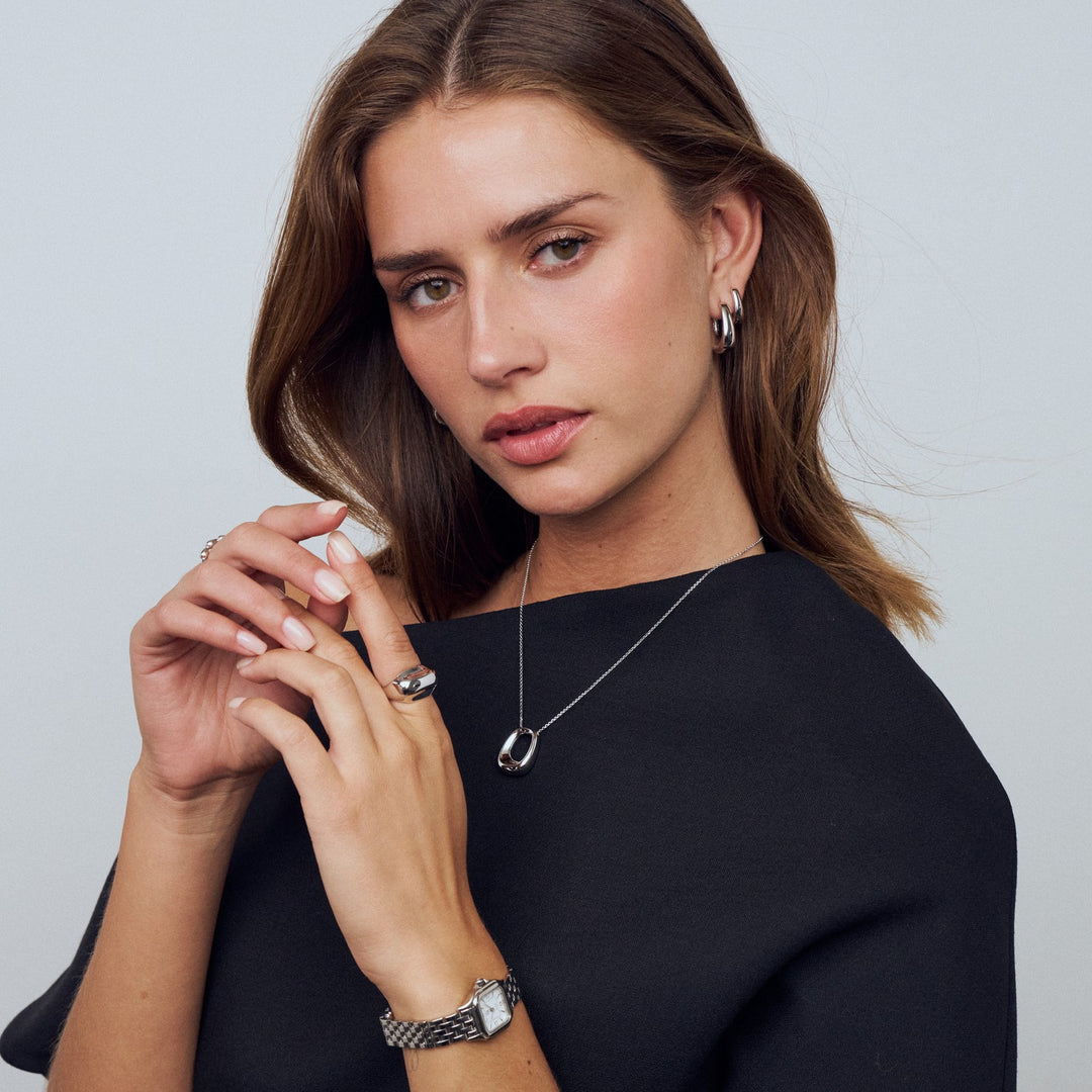 Woman wearing jewelry including a necklace, earrings, and rings on a plain background