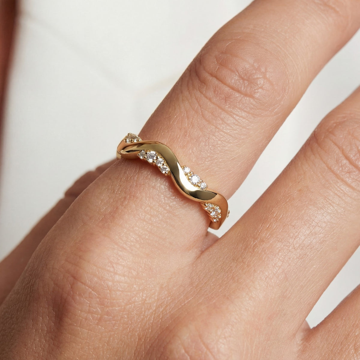 Gold ring with diamonds on a finger against a neutral background