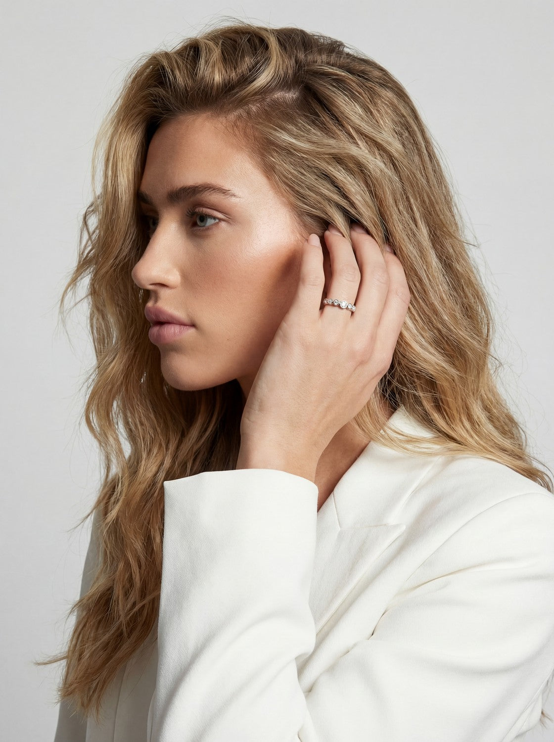 Woman with blonde hair touching her ear against a plain background