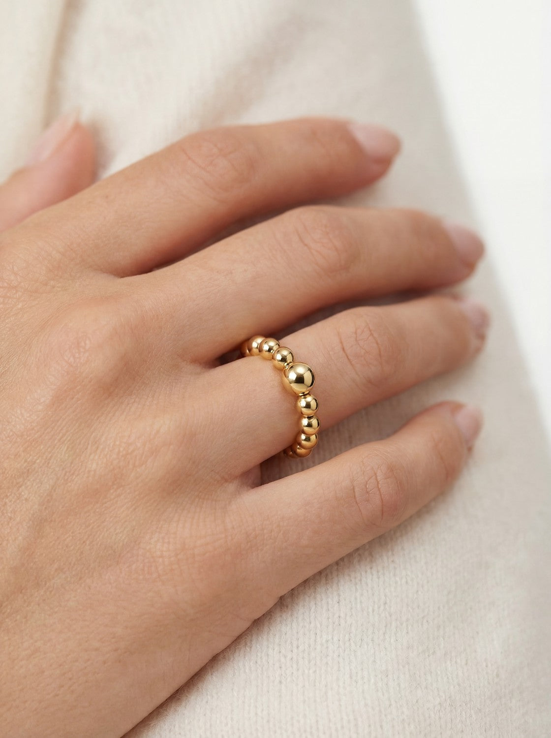 Gold beaded ring on a hand against a neutral background