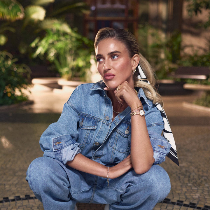 Woman in a denim outfit sitting outdoors with plants in the background