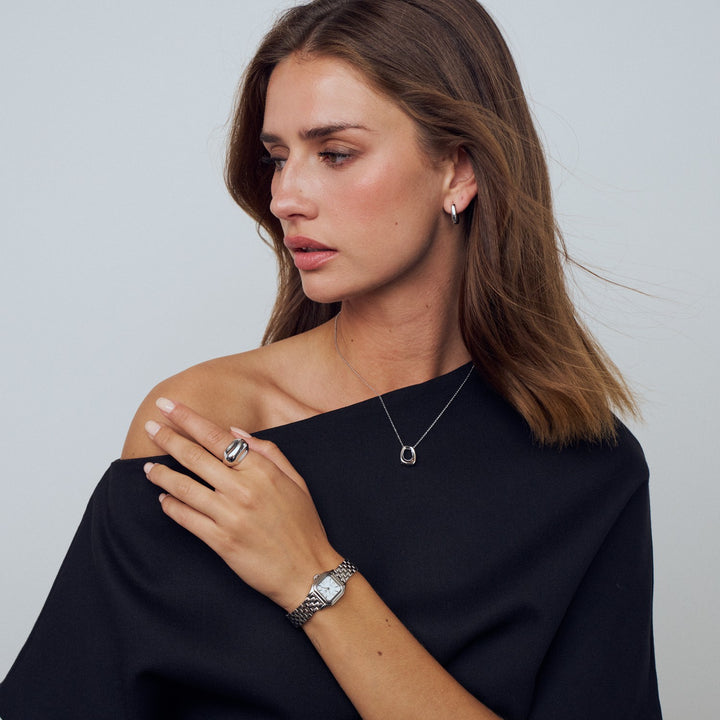 Woman wearing a black top with jewelry including a ring, bracelet, and necklace against a plain background