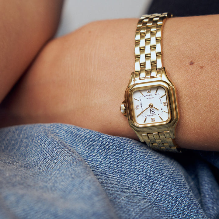 Gold wristwatch on a person's wrist with a denim background