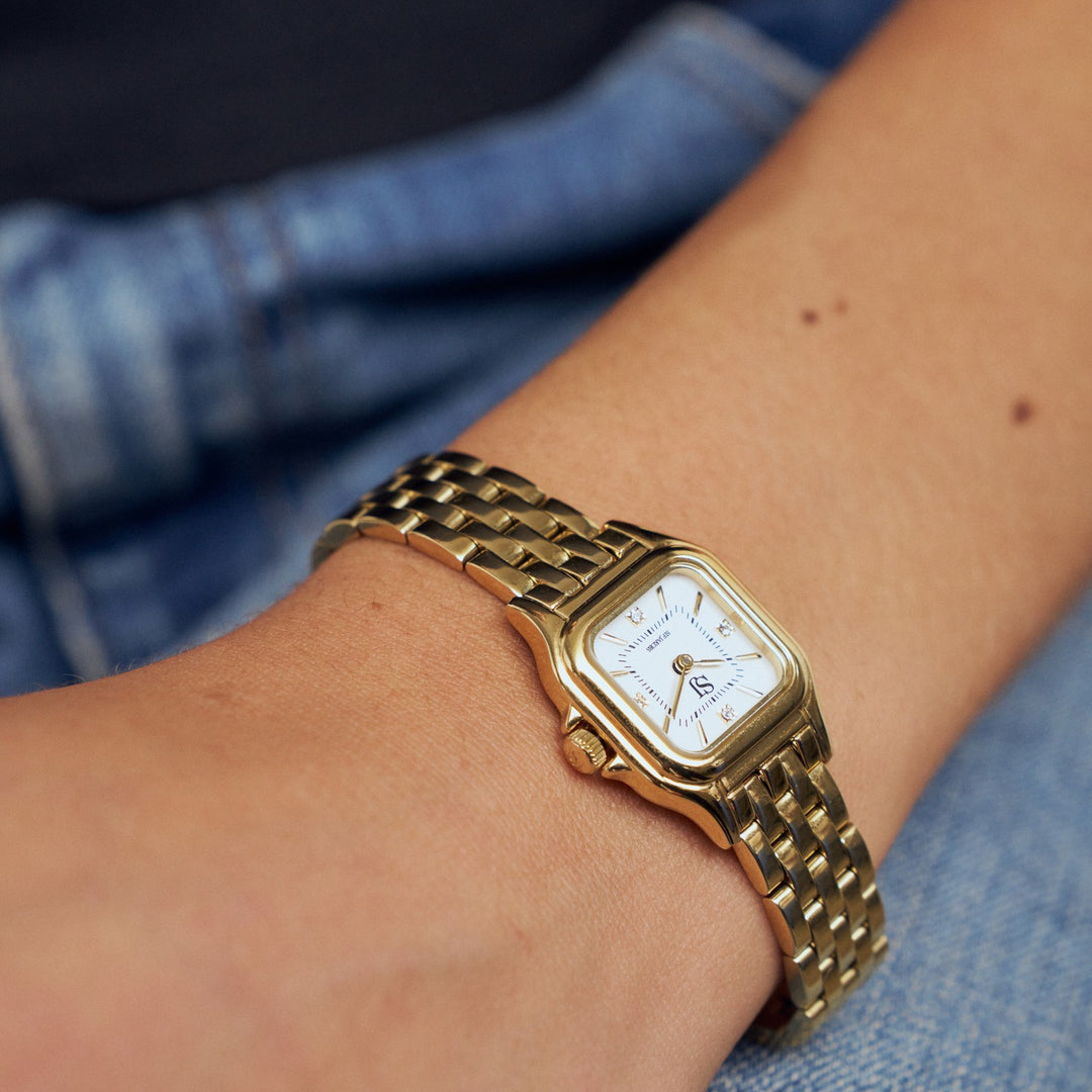Gold wristwatch on a person's wrist with a blue denim background