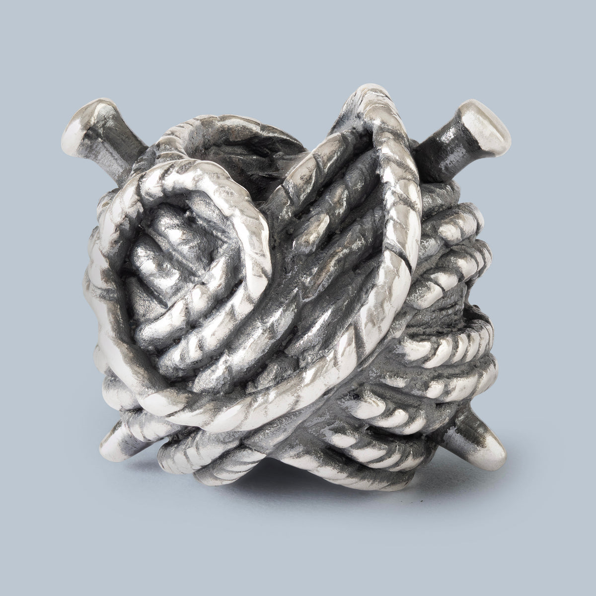 Silver knot charm with two nails on a light gray background