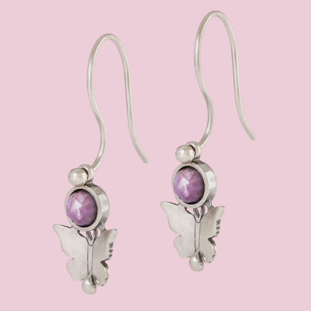 Butterfly-shaped earrings with purple gemstones on a pink background