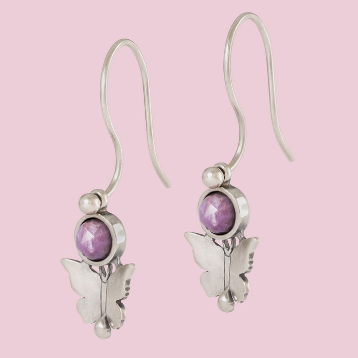 Butterfly-shaped earrings with purple gemstones on a pink background