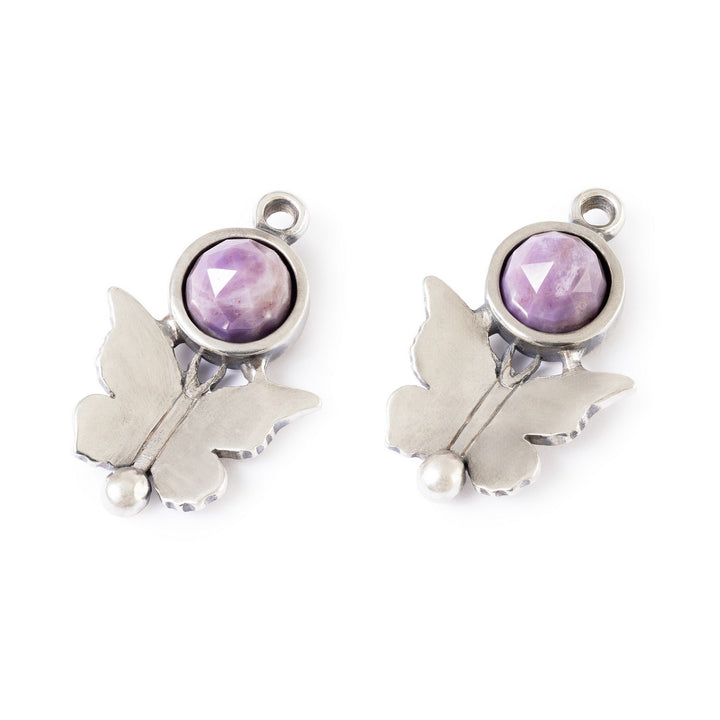 Butterfly-shaped silver charms with purple gemstones on a white background