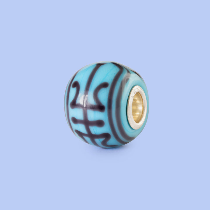 Turquoise glass charm with gold core on a light blue background