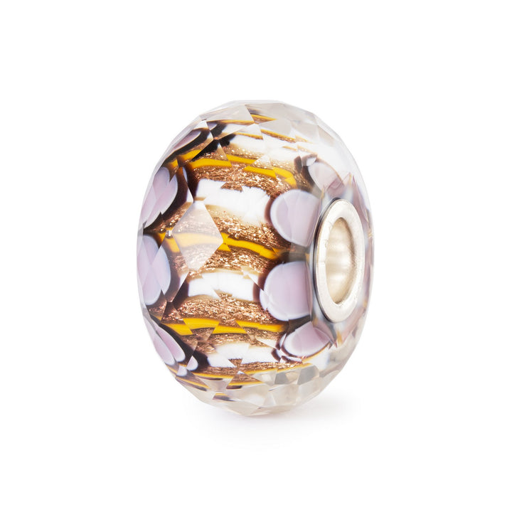 Decorative glass bead with purple and gold patterns on a white background