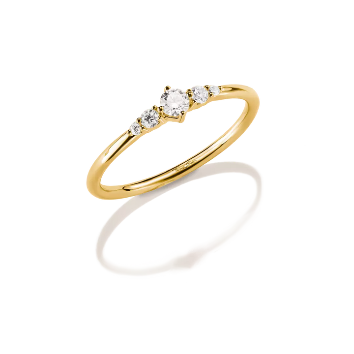 A yellow gold ring with a three-stone diamond setting, photographed on a clean white background with a soft reflection underneath.