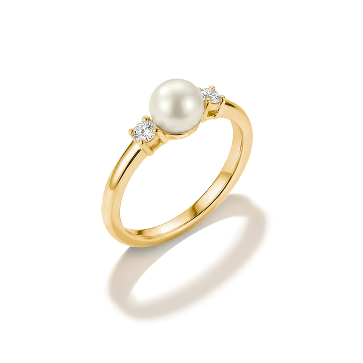 A yellow gold ring featuring a central white pearl flanked by two small clear diamonds, set against a clean white background with a soft shadow.
