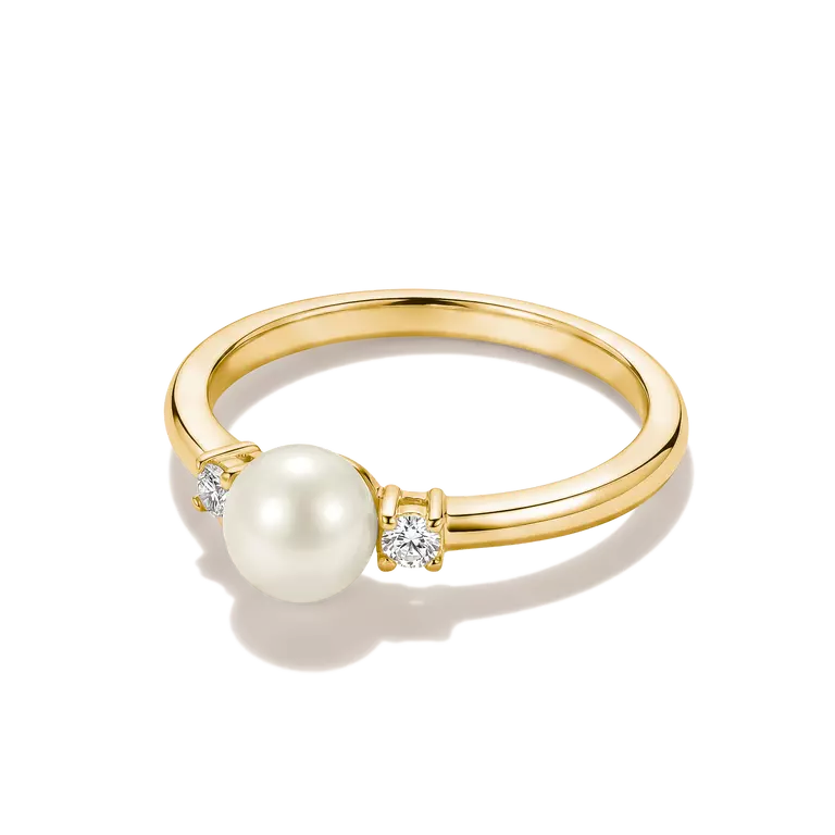 A yellow gold ring featuring a large white pearl and two small clear diamonds, set on a clean white background with a soft shadow.