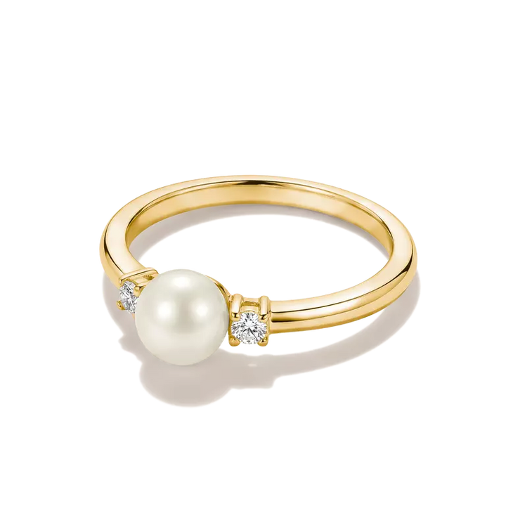 A yellow gold ring featuring a large white pearl and two small clear diamonds, set on a clean white background with a soft shadow.