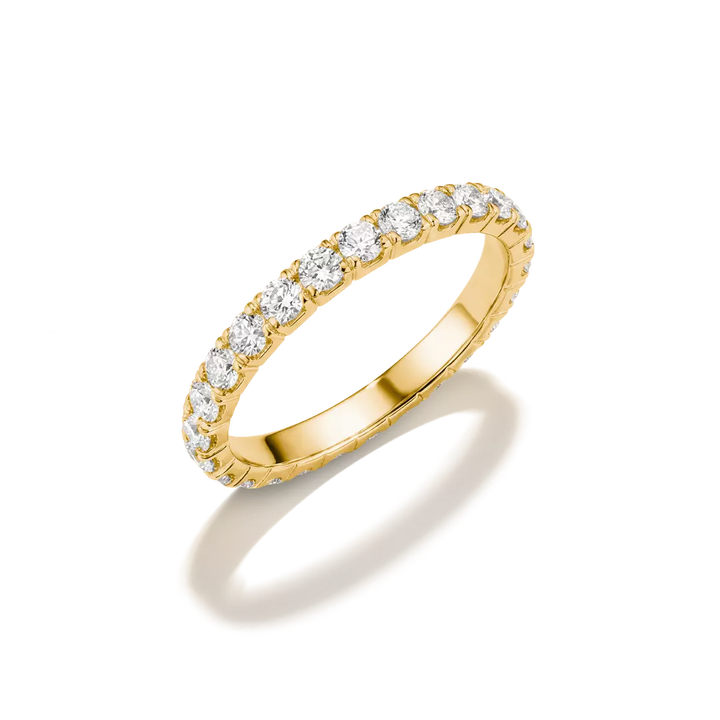 A yellow gold eternity ring featuring a continuous row of round-cut clear gemstones, shown on a clean white background with a soft shadow.