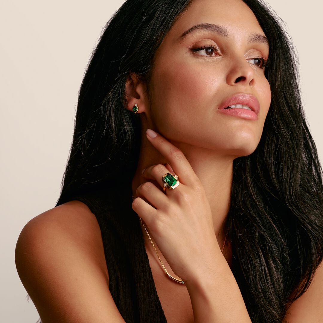 Woman wearing a green gemstone ring and earrings on a beige background