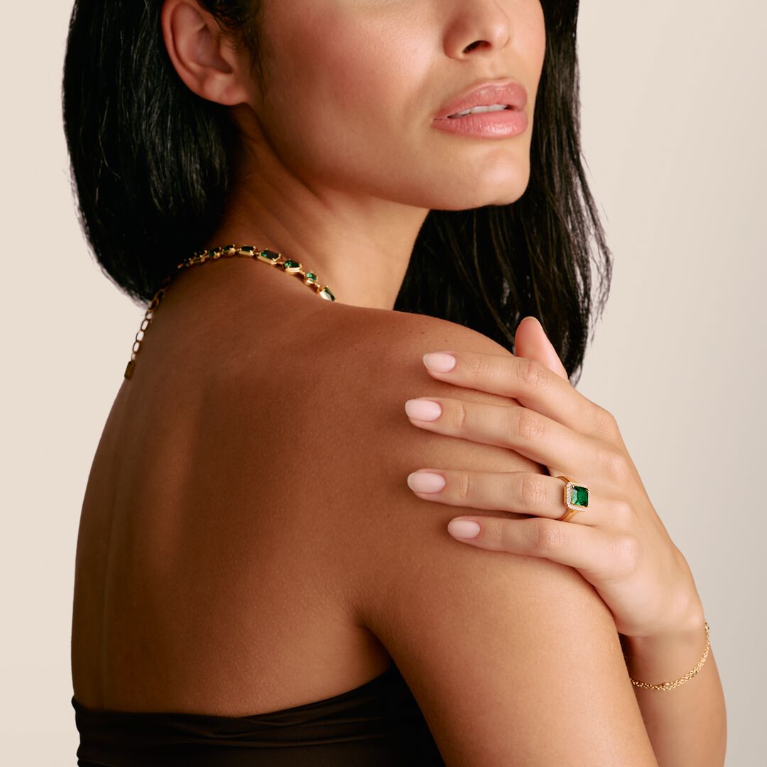 Woman wearing gold jewelry with green gemstones on a neutral background
