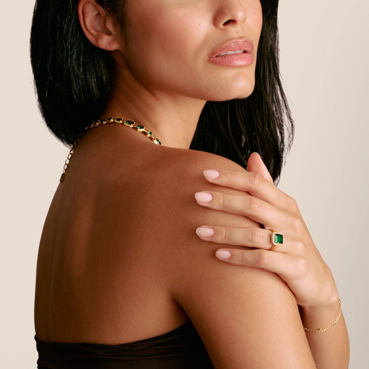 Woman wearing gold jewelry with green gemstones on a neutral background