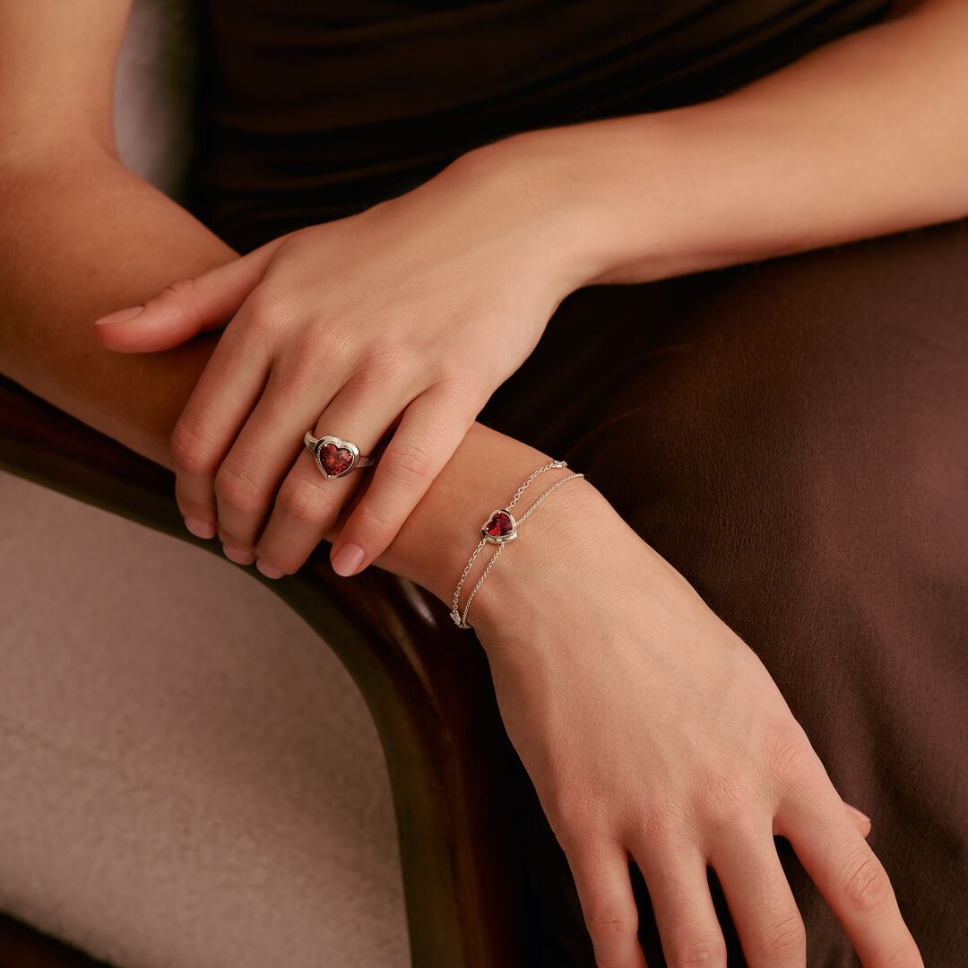 Close-up of hands wearing a ring and bracelet with red gemstones on a brown background