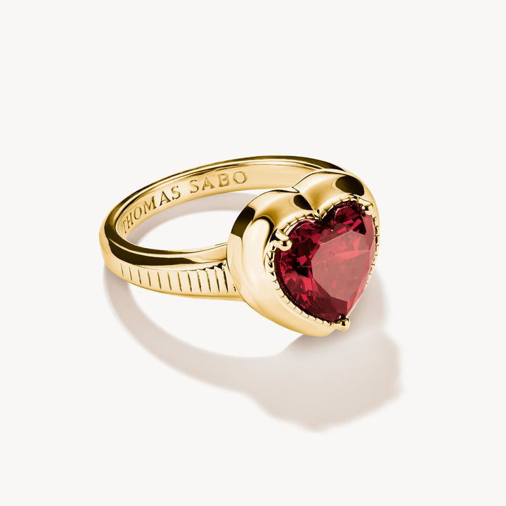 Gold ring with a red heart-shaped gemstone on a white background