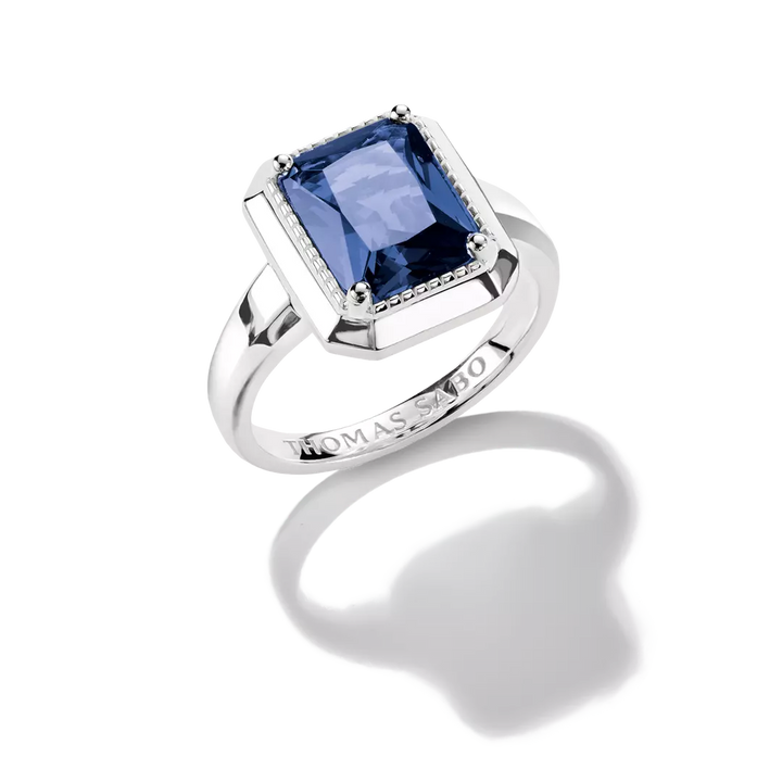 A Thomas Sabo ring featuring a rectangular cushion-cut blue sapphire gemstone in a silver-toned bezel setting with small pavé accents, shown on a white background with a soft reflection.
