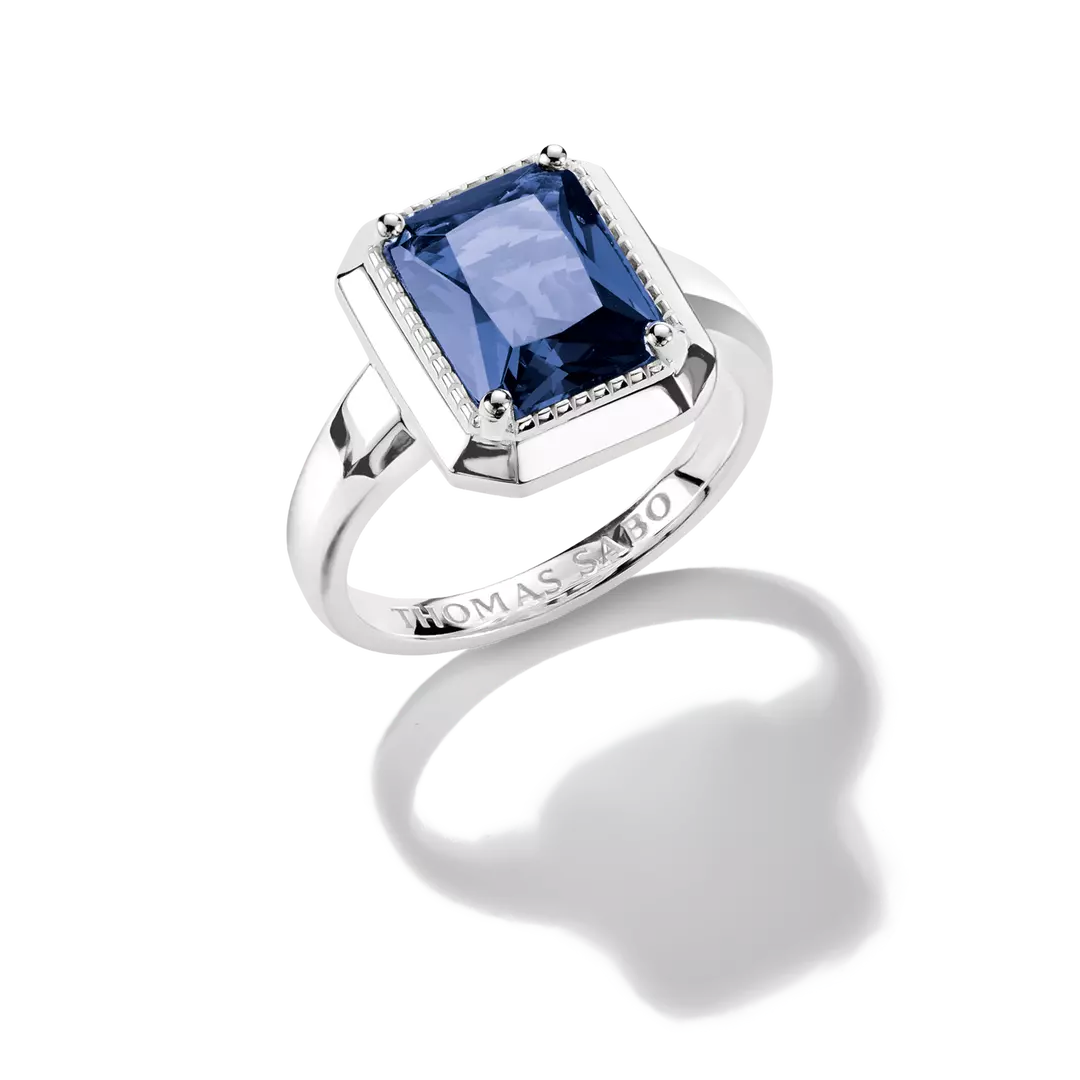 A Thomas Sabo ring featuring a rectangular cushion-cut blue sapphire gemstone in a silver-toned bezel setting with small pavé accents, shown on a white background with a soft reflection.
