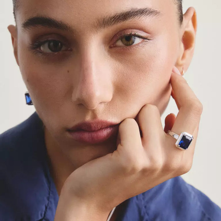 A Thomas Sabo ring featuring a rectangular cushion-cut blue sapphire gemstone in a silver-toned bezel setting with small pavé accents, shown on a white background with a soft reflection.