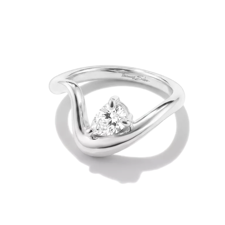 A silver engagement ring featuring a triangular-cut diamond set in a sculptural, flowing band, photographed on a clean white background with a soft shadow.