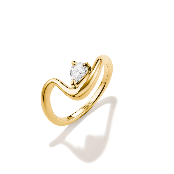 A yellow gold ring with a curved, wave-like band and a pear-cut clear gemstone in the center, shown on a clean white background with a soft shadow.