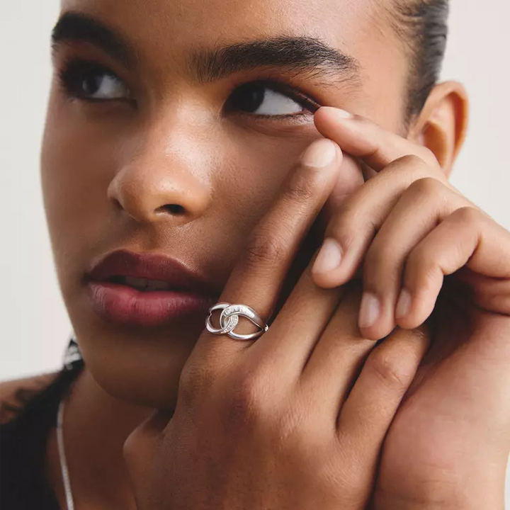 A close-up lifestyle shot of a model wearing a silver ring with two interlocking oval shapes on her finger.