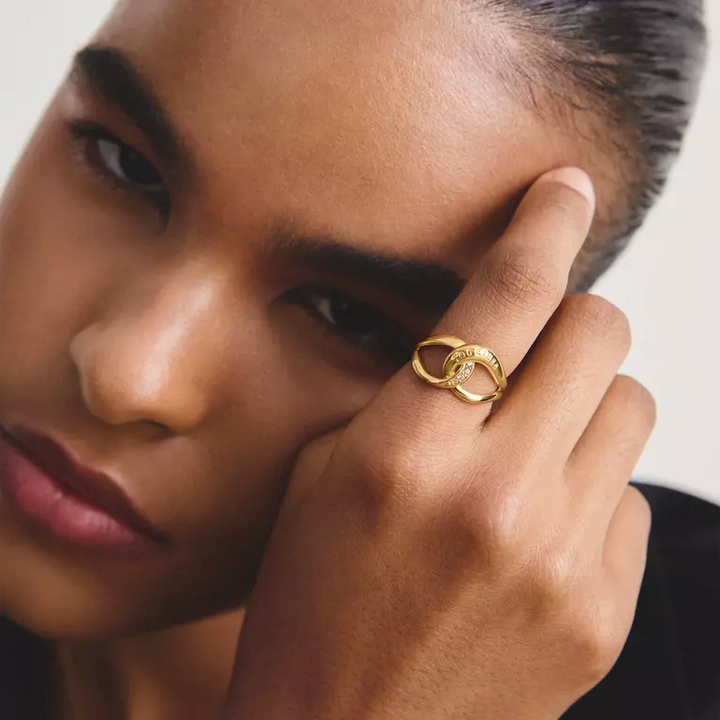 A gold interlocking rings ring with a small clear stone accent and 'TOGETHER' engraved on the top, and 'THMAS SABO' on the band, shown on a white background with a soft shadow.