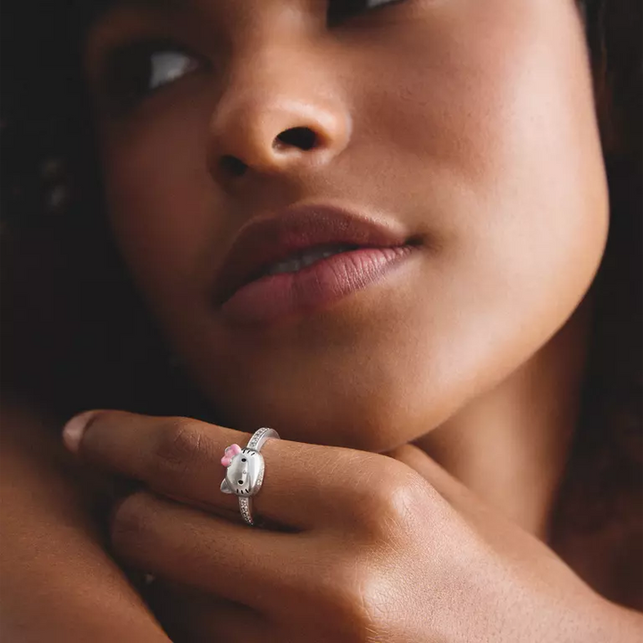 A close-up lifestyle shot of a model wearing a silver Hello Kitty ring on her finger. The ring features a silver Hello Kitty face with a small pink bow.
