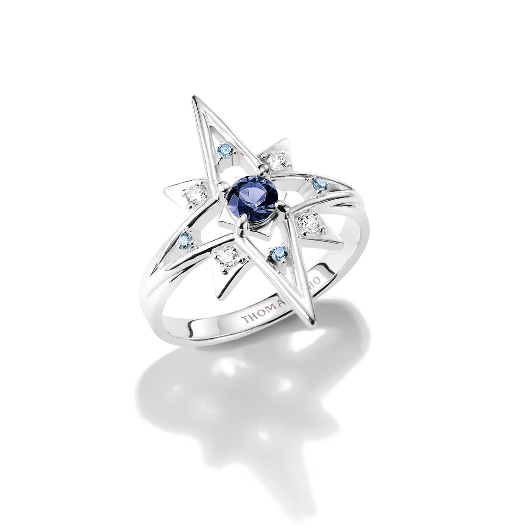 A silver star-shaped ring featuring a central deep blue gemstone and small light blue accent stones, photographed on a clean white background with a soft reflection.