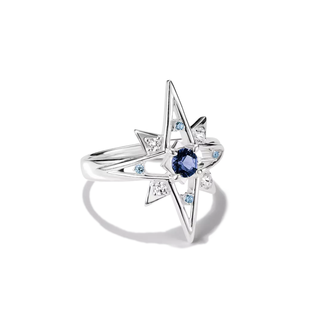 A silver starburst ring featuring a central round blue sapphire and small light blue and clear accent stones, shown on a clean white background.
