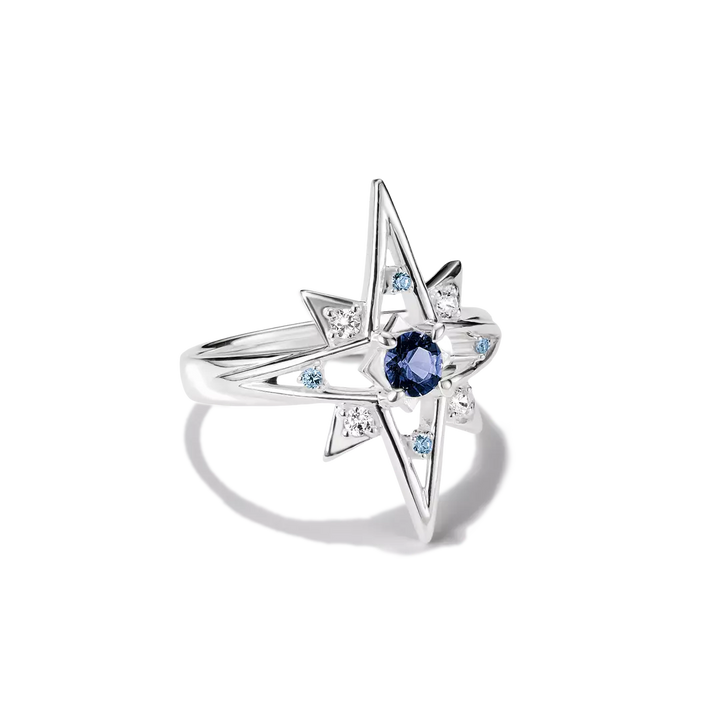 A silver starburst ring featuring a central round blue sapphire and small light blue and clear accent stones, shown on a clean white background.