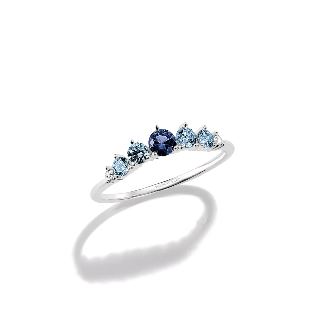 A silver five-stone ring featuring one dark blue oval center stone and four light blue marquise-cut side stones, displayed on a clean white background with a soft shadow.
