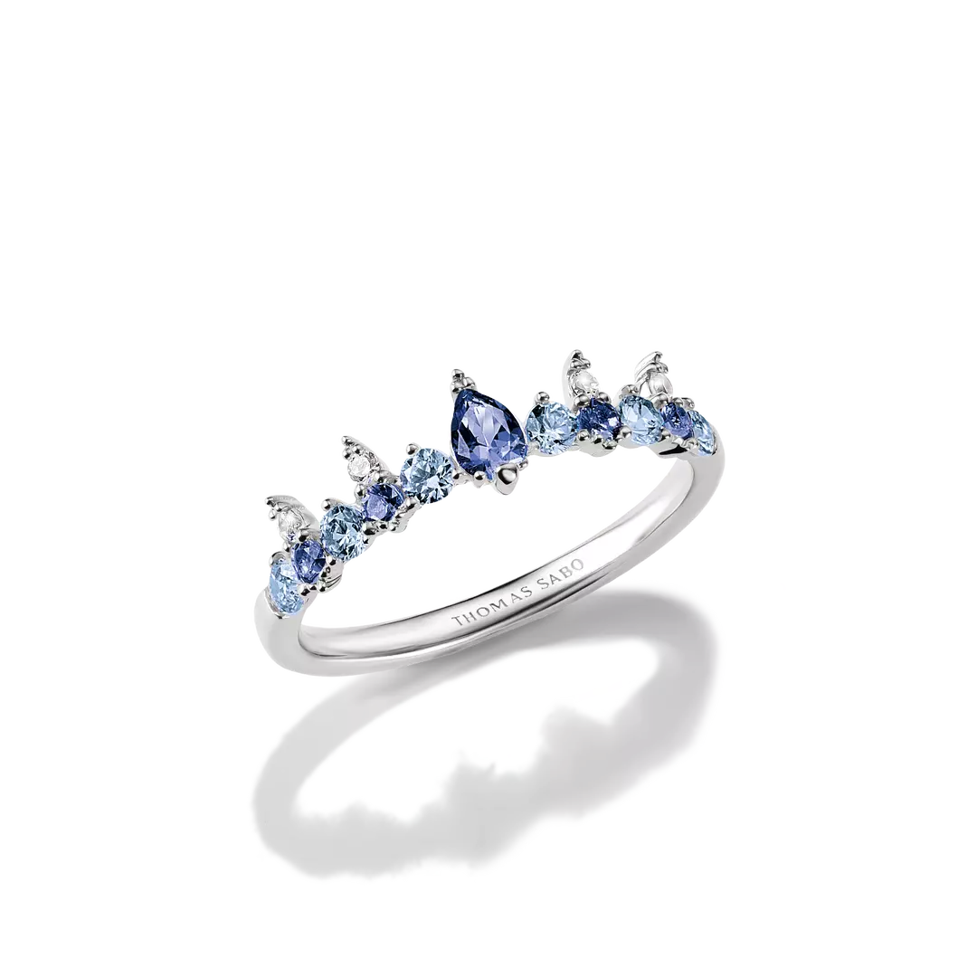 A silver-tone ring featuring a row of light blue and deep blue gemstones, including a central marquise-cut blue stone, set against a clean white background with a soft reflection.