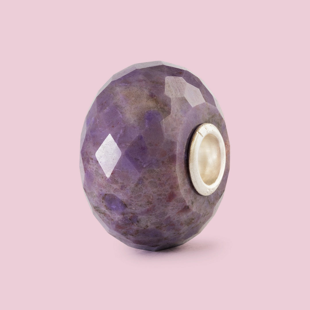 Faceted purple bead with a white center on a pink background