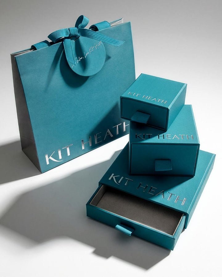 Teal Kit Heath gift packaging set including a large shopping bag with a ribbon, a stack of three nested boxes, and an open drawer box on a white studio background.