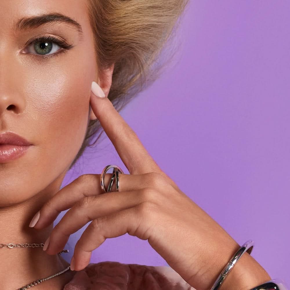 Close-up of a model wearing a sterling silver trio ring, highlighting its luxurious design against a pastel purple background.